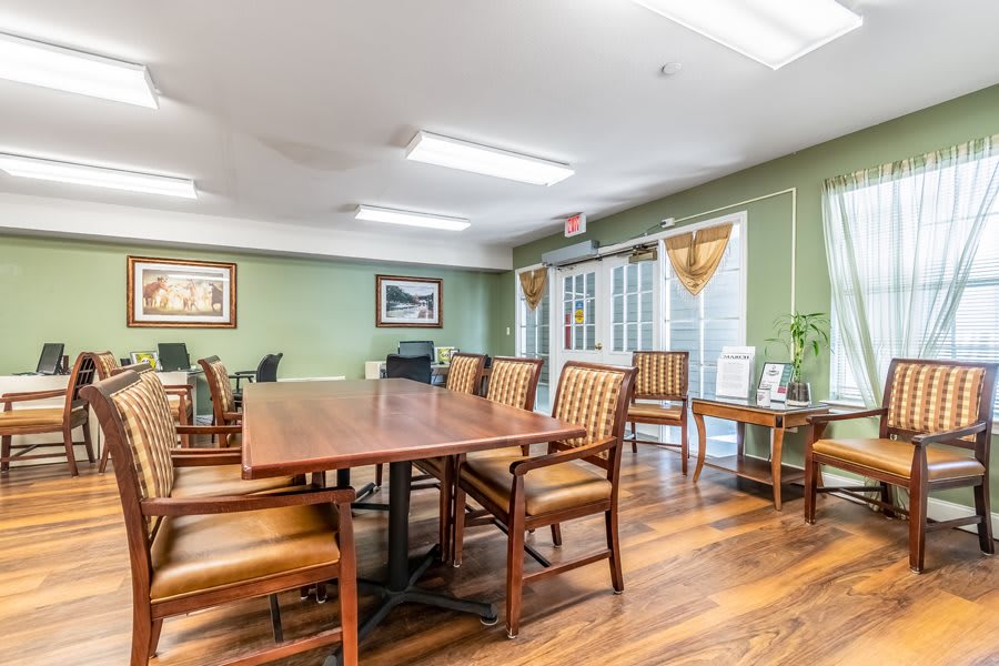A well-lit conference room with a large wooden meeting table and chairs, featuring green walls and artwork.