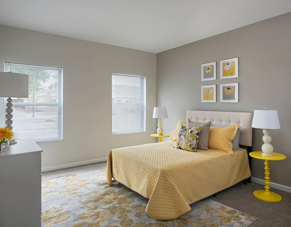 A modern bedroom featuring a neutral gray and yellow color scheme, with natural light streaming through the windows.