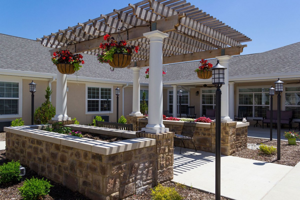A charming patio area with a pergola and hanging plants, featuring a stone wall and a lamp post.