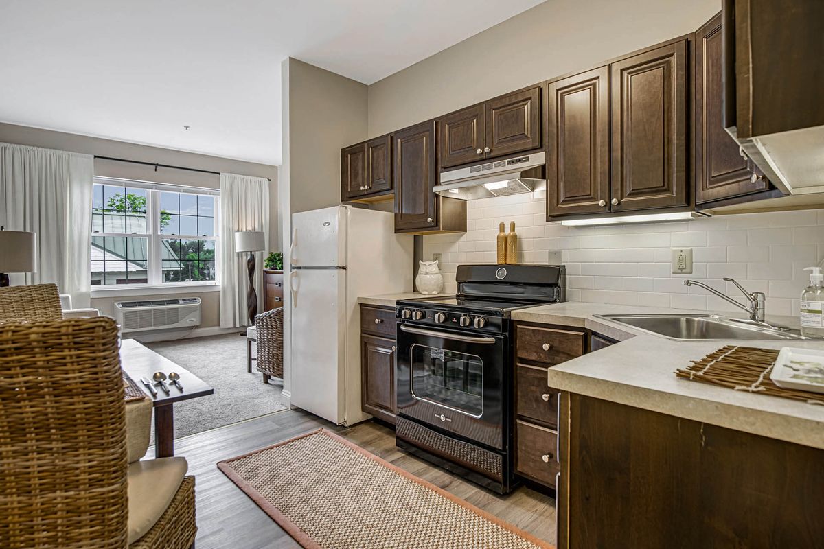 A modern apartment kitchen with wooden cabinets and a view into the living room.