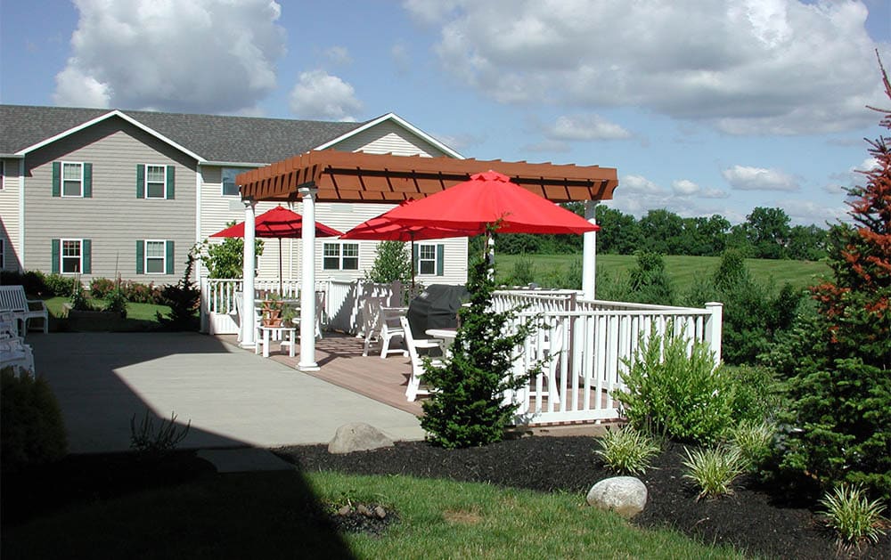 A cozy outdoor patio with red umbrellas and a pergola next to a house.