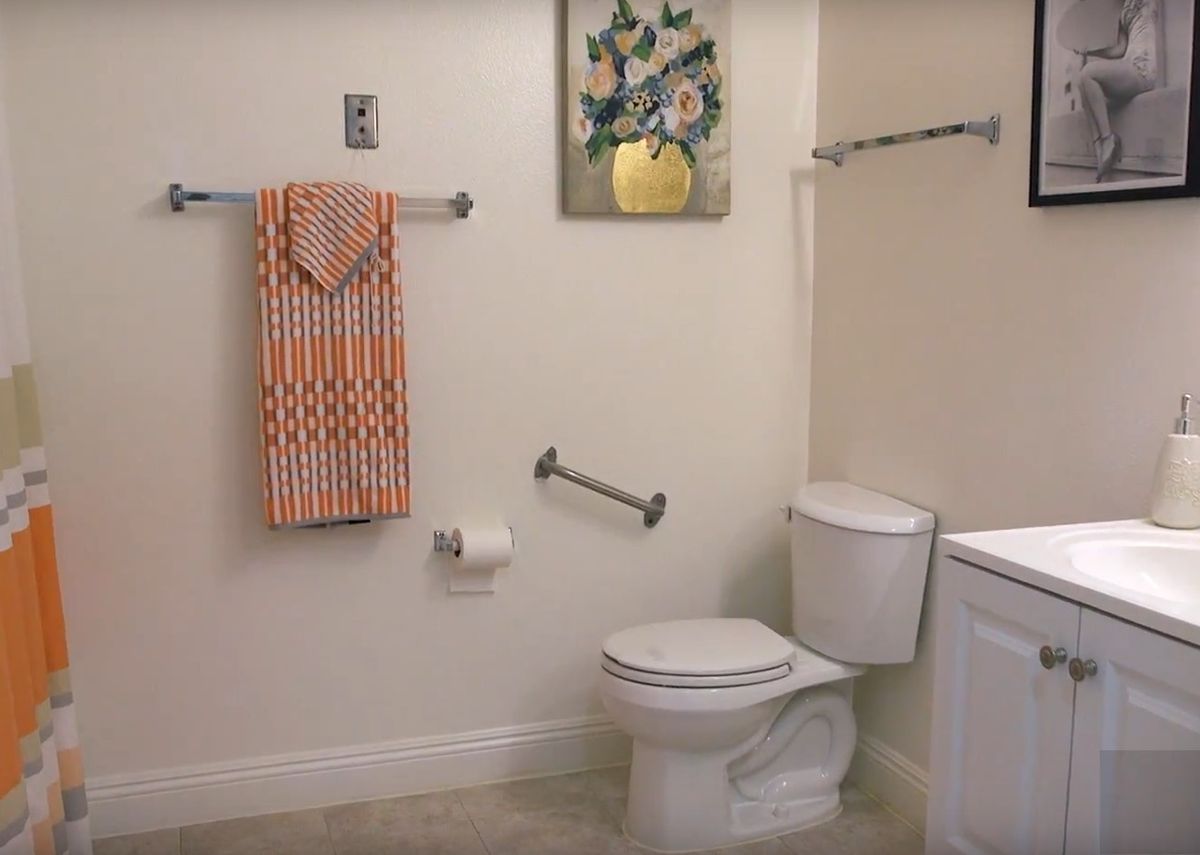 A well-organized bathroom featuring a toilet, towels on a rack, a painting, and handrails for accessibility.