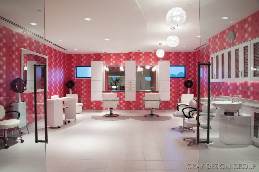 A modern hair salon with pink patterned walls, stylish chairs, and mirrors.