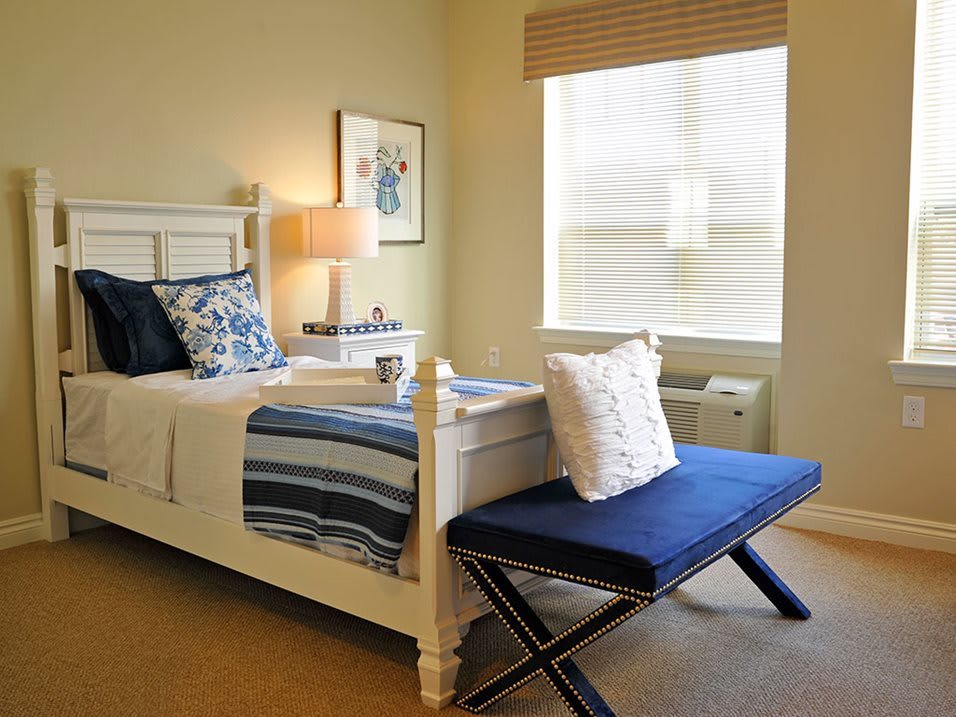 A well-decorated bedroom with a neatly made bed, blue accents, and natural lighting.