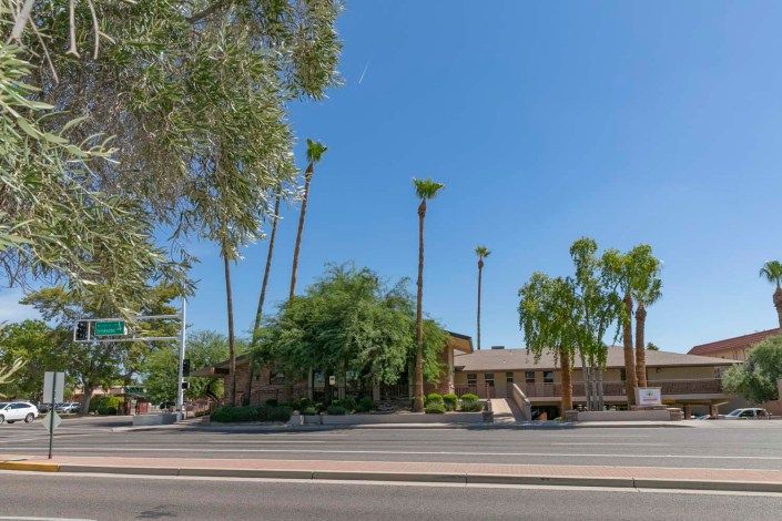 A sunny day view of a building surrounded by palm trees along a street.