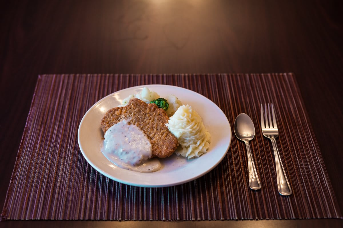 A plate of chicken fried steak with gravy alongside mashed potatoes, set on a dining table.