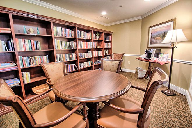 A cozy library room with bookshelves and a wooden table surrounded by chairs.