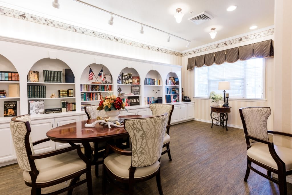 A cozy reading room with a round table and chairs, surrounded by built-in bookshelves filled with books and decorative items.