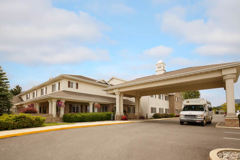 A building with an entrance canopy and a vehicle parked in front under a partly cloudy sky.