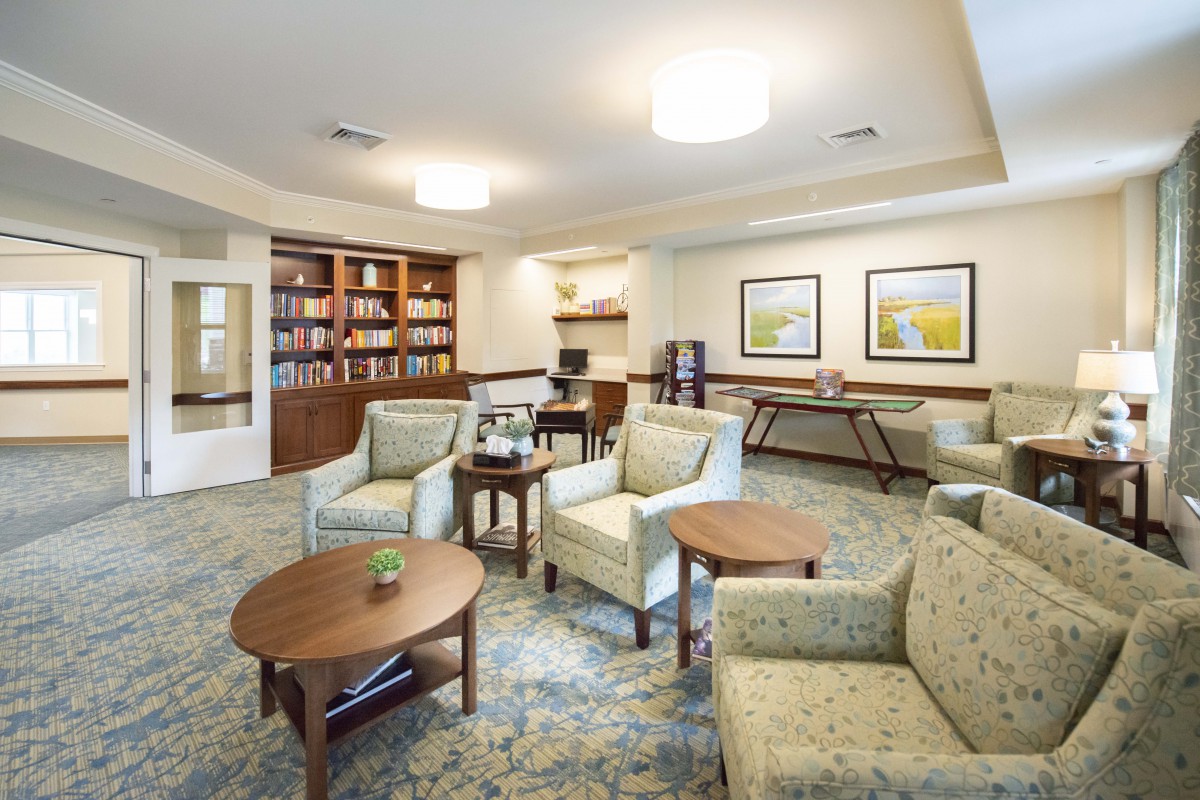 A cozy living room area with comfortable chairs, a central table, bookshelves, and warm lighting.