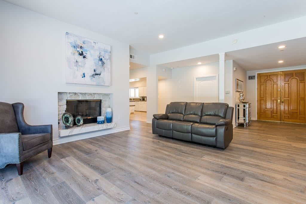 A modern living room with a leather couch, fireplace, and wood flooring, featuring minimalist decor and artwork.