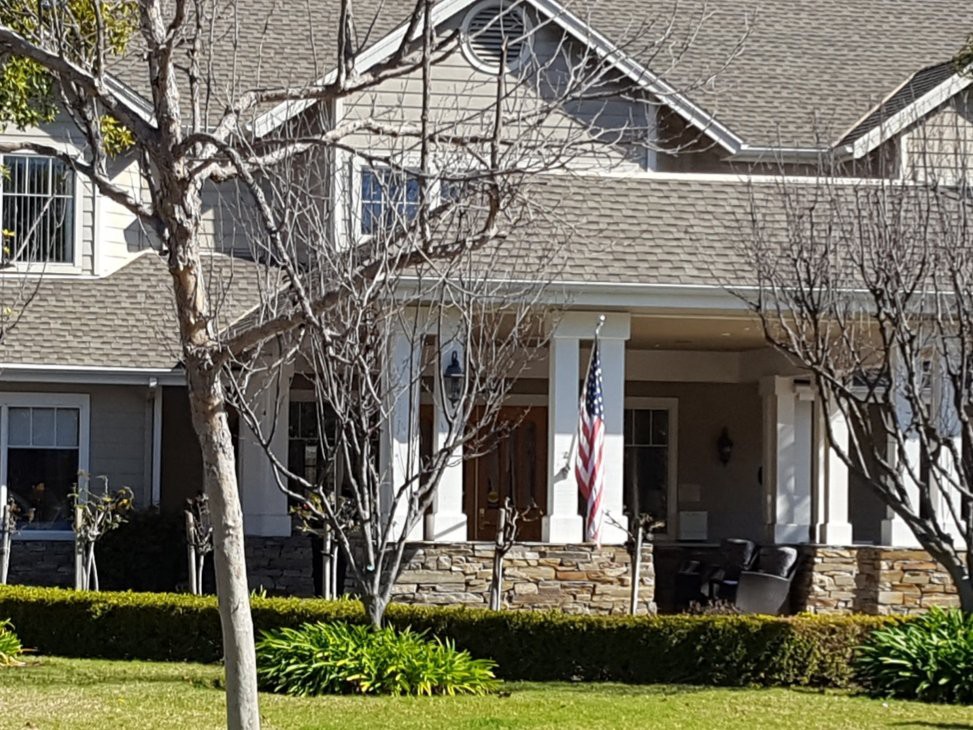 A suburban house with a front porch and well-maintained yard, featuring trees and shrubs.