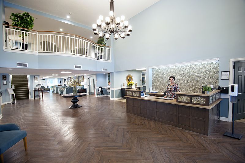 A spacious and modern hotel lobby with a reception desk, elegant chandelier, and stylish flooring.