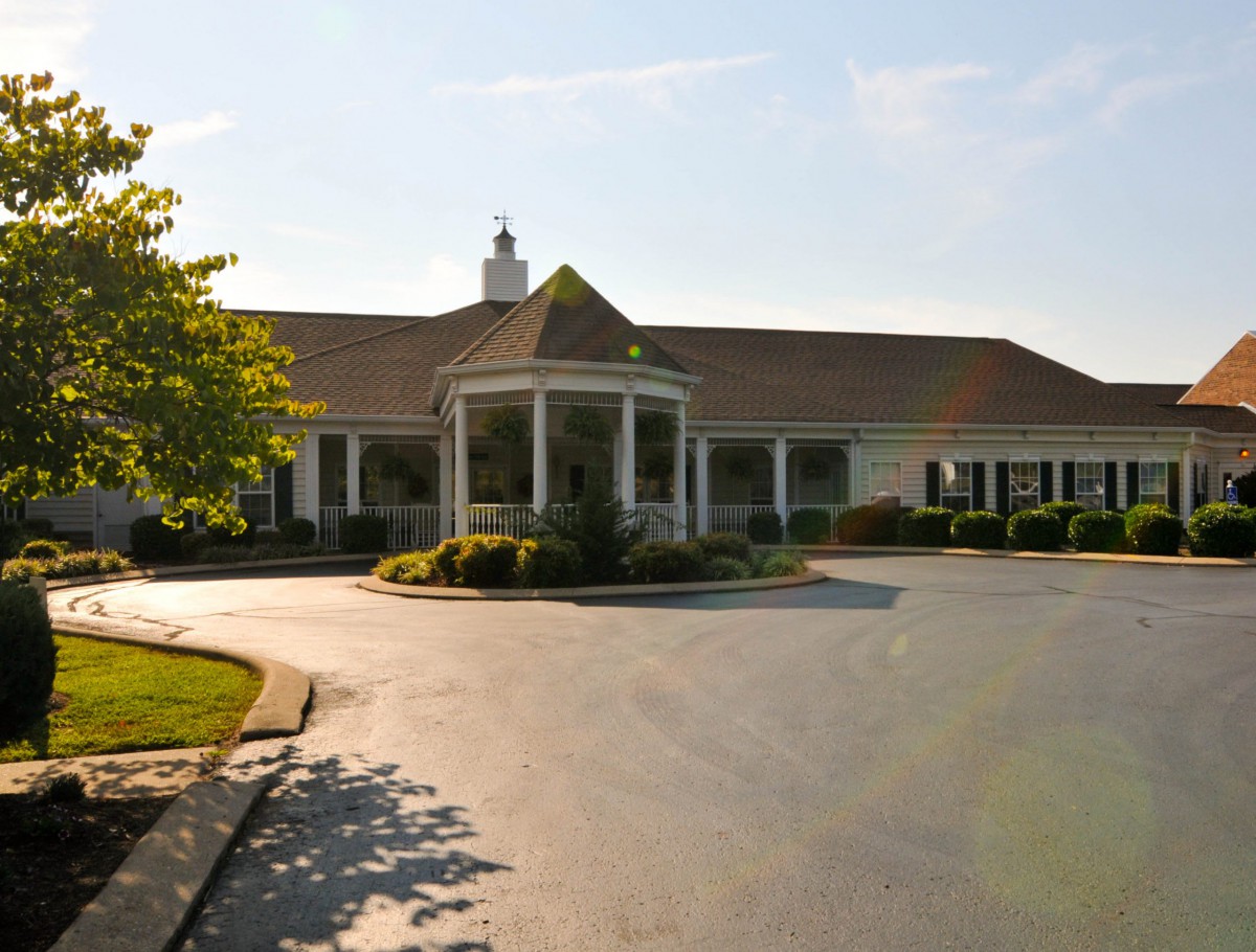 A large building with a circular driveway, surrounded by greenery under a sunny sky.