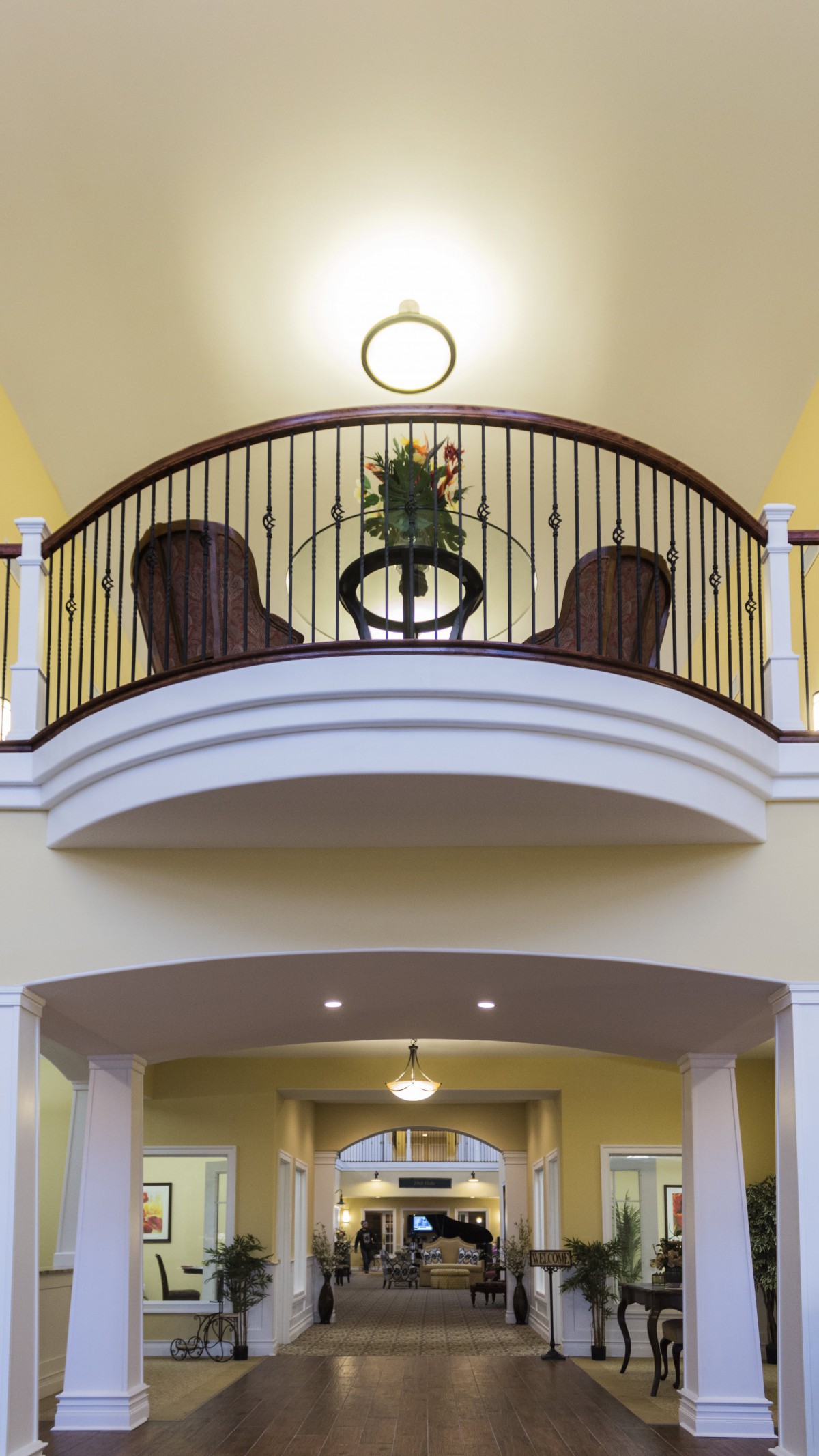 An interior balcony with a decorative railing, featuring two chairs and a small table with a plant.