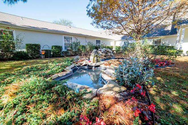 A serene garden with a small pond surrounded by lush greenery and vibrant flowers.