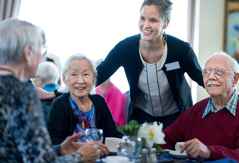 A caregiver interacts warmly with seniors at a group gathering.