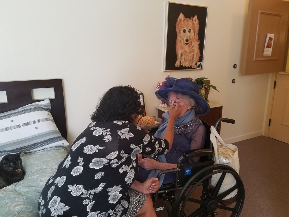 A caregiver assists an elderly person in a wheelchair within a home setting.