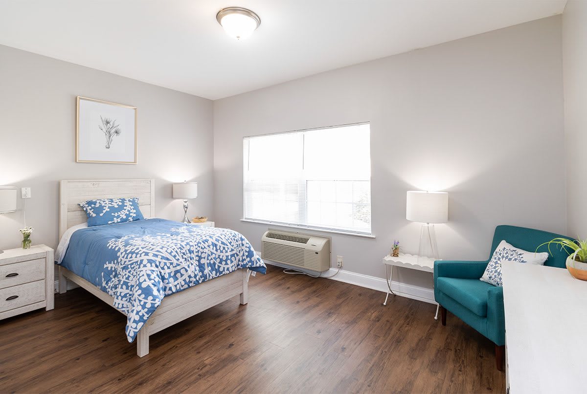A well-lit modern bedroom featuring a bed with patterned bedding, two lamps, and a comfortable chair.