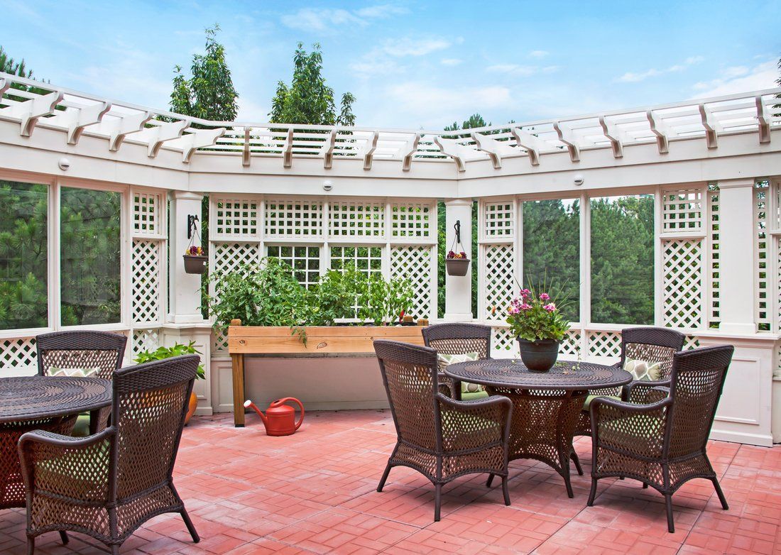 A cozy outdoor patio with a pergola, featuring a dining table and chairs surrounded by planter boxes.