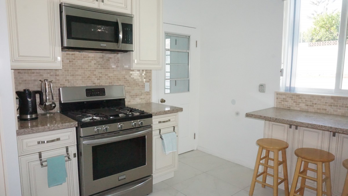 A modern kitchen with a stove, microwave, and bar stool.