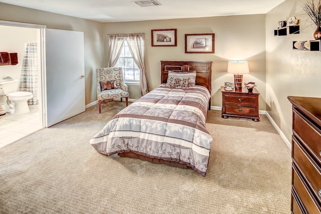 A cozy bedroom with a single bed, framed pictures, and a nightstand lamp.