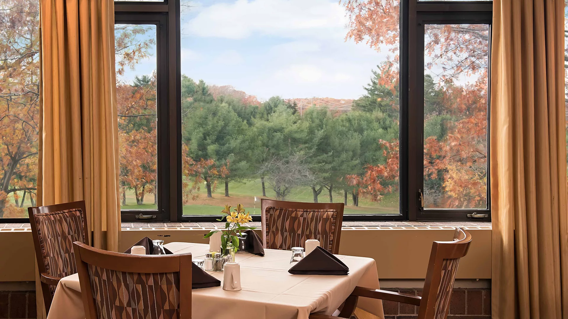 A cozy dining area with a scenic view of autumn trees through large windows.