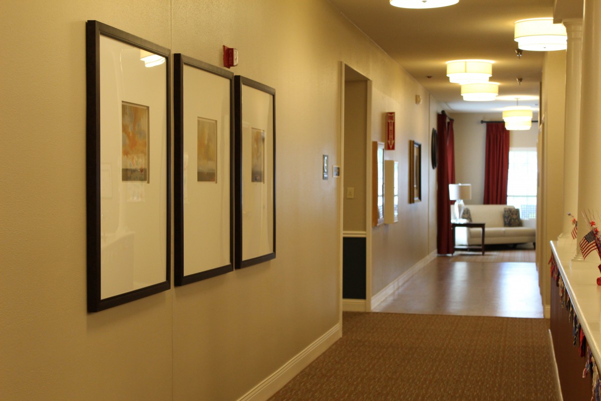 A hallway with framed artwork on the walls and a glimpse of furniture in the adjacent room.