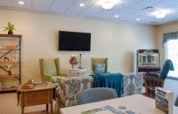 A cozy living room with comfortable chairs, a table, and a television on the wall.