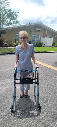 An elderly woman using a walker to assist her while walking outdoors.