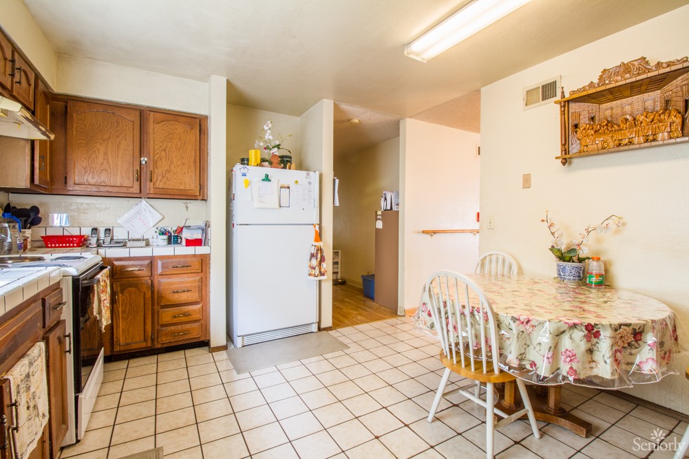 A cozy kitchen and dining area with wooden cabinets, a refrigerator, tile flooring, and a small table with chairs.