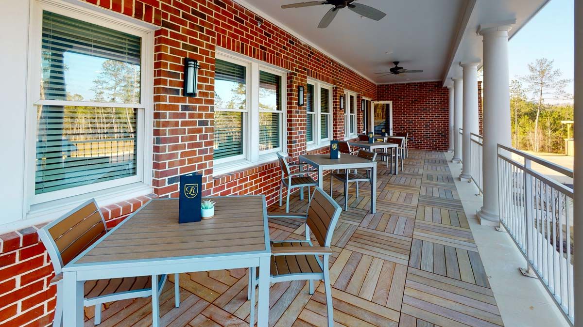 A cozy outdoor patio with tables and chairs lined against a brick wall, featuring ceiling fans for comfort.