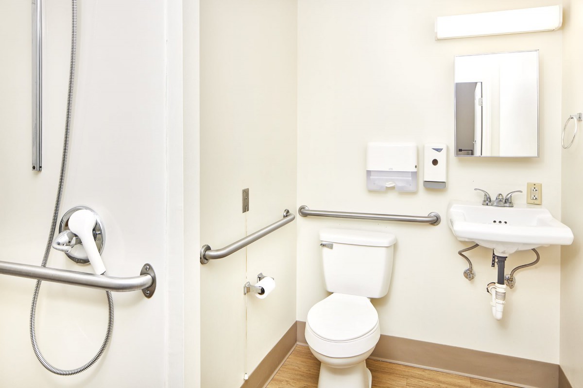 An accessible bathroom with a toilet, sink, and handrails.