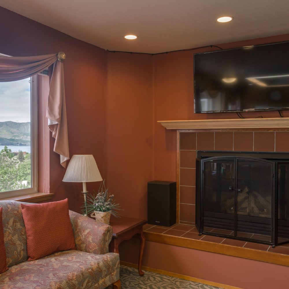A cozy living room with a fireplace, TV mounted above it, and a sofa by the window.