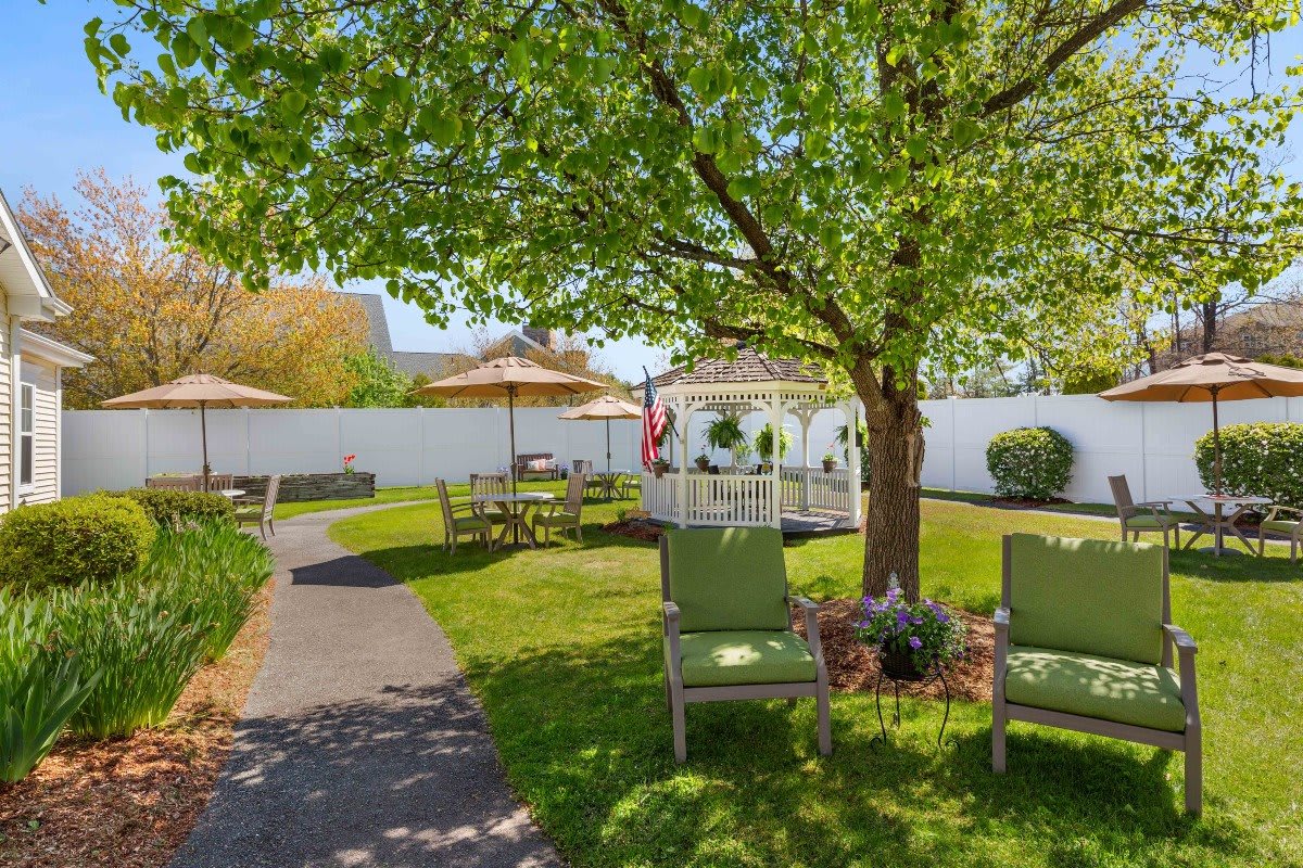 A tranquil garden setting with chairs under a tree and patio furniture in the background.