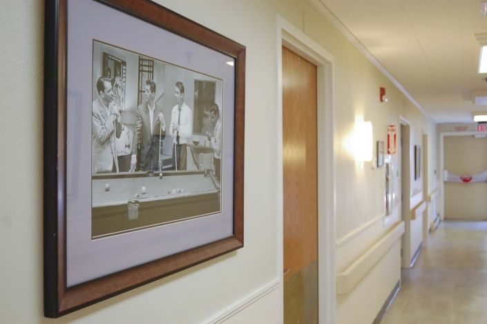 A hallway featuring a framed black-and-white photograph on the wall, with doors and lighting along the corridor.