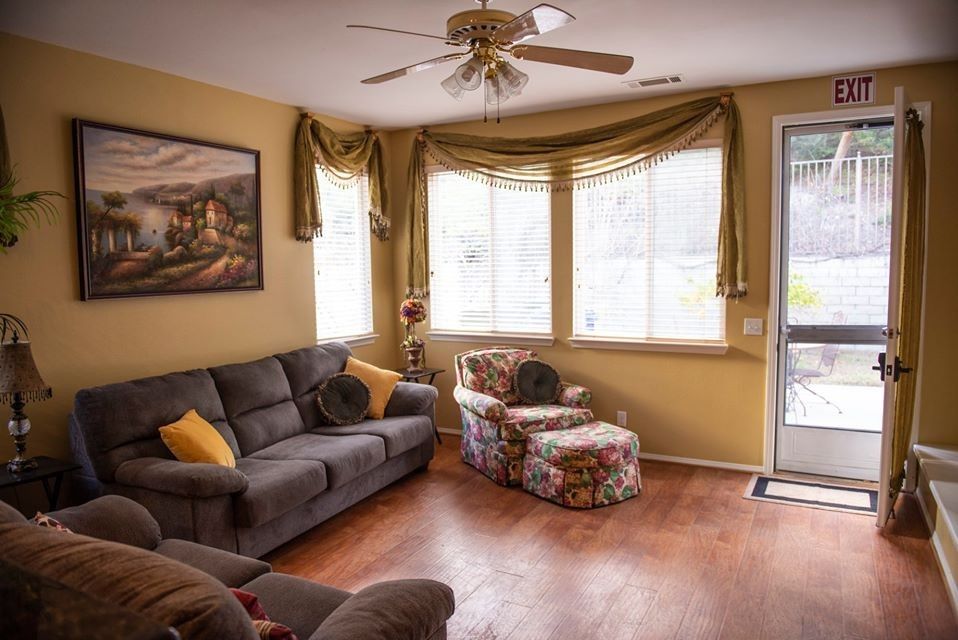 A cozy living room with a gray sofa, floral armchair, and large windows letting in natural light.