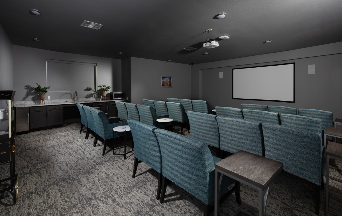 A cozy theater-style room with teal seating arranged in rows facing a large projector screen.