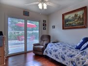 A cozy bedroom featuring a bed with a blue and white quilt, a recliner chair, and large French doors opening to a patio with an umbrella.