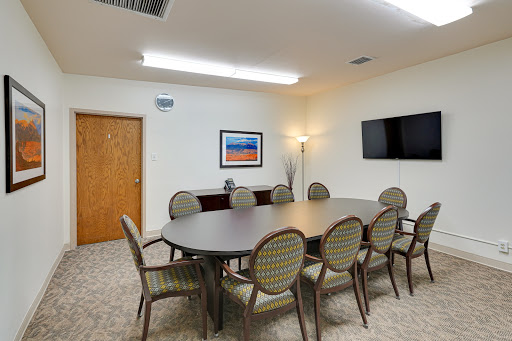 A well-furnished meeting room featuring a large conference table surrounded by chairs, equipped with wall art and a television.