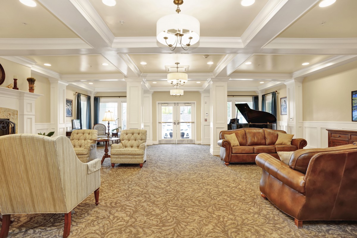 An elegant living room with plush sofas, armchairs, and a grand piano, illuminated by chandeliers.