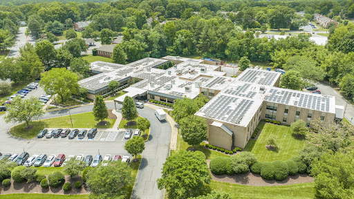 An aerial view of a modern building featuring solar panels surrounded by lush greenery.