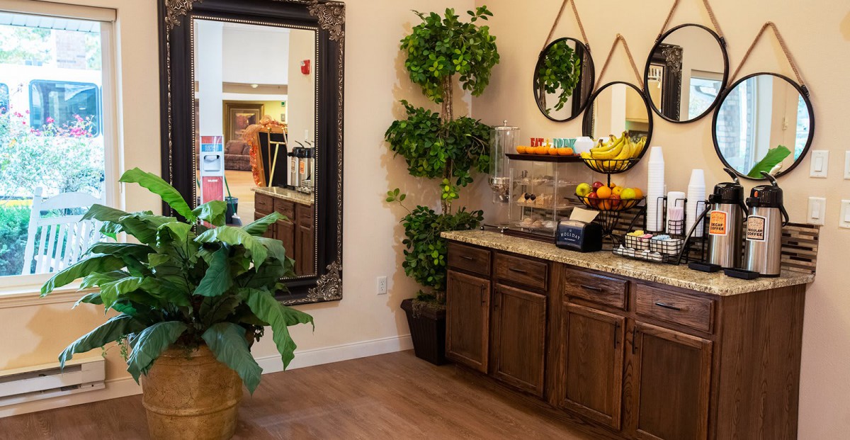 A cozy corner in a kitchen featuring plants, a large mirror, and a fruit-laden counter.