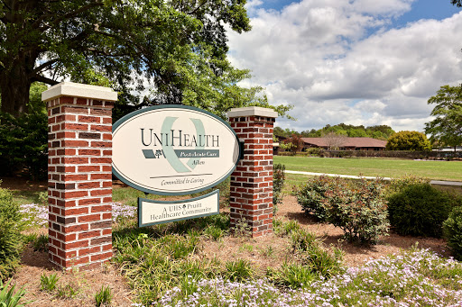 Entrance sign of UniHealth surrounded by landscaped greenery and a cloudy sky.