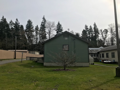 A green house set against a backdrop of trees and an open grassy area.