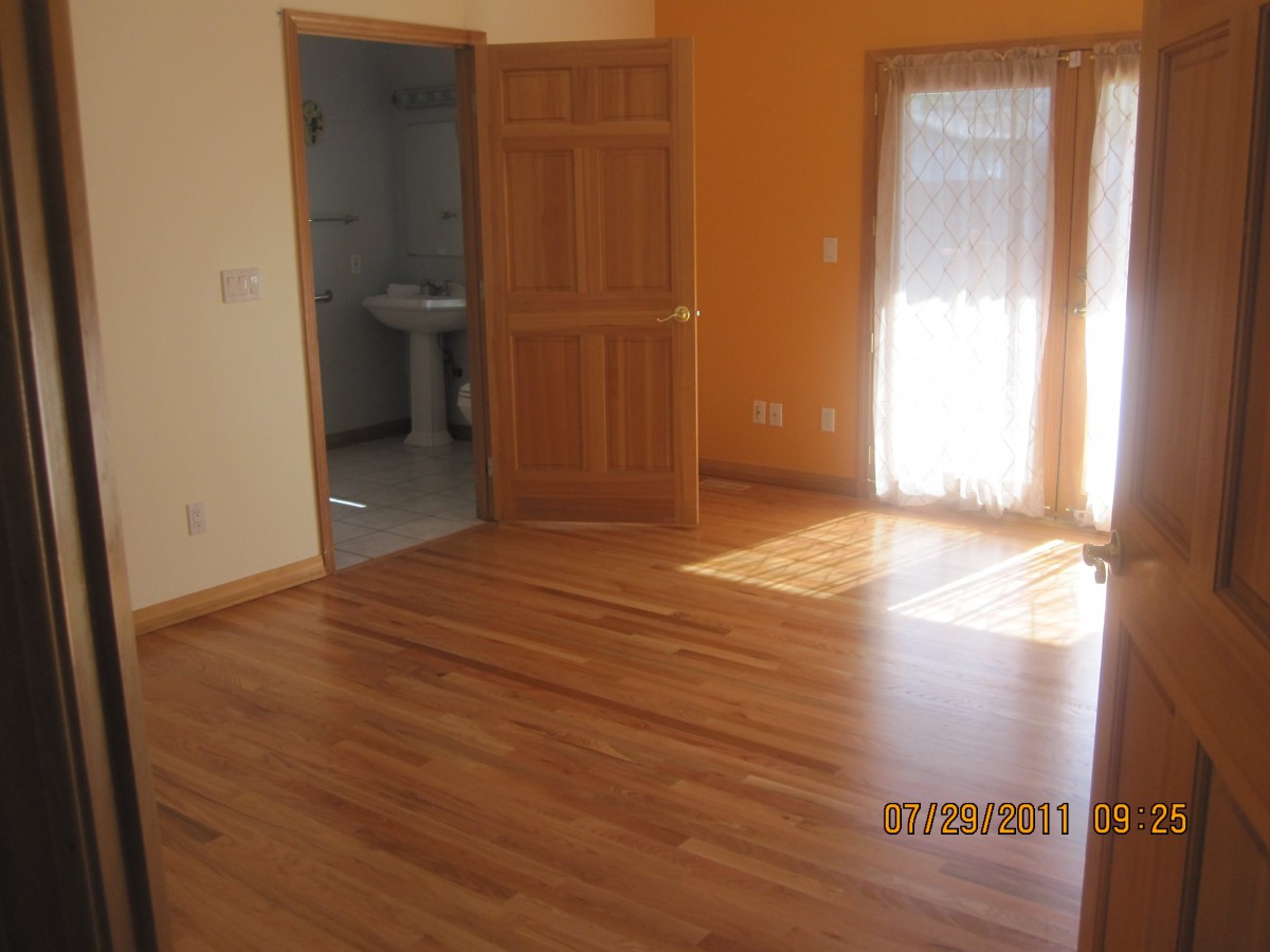 An empty room with wooden flooring and sunlight streaming through the doors.