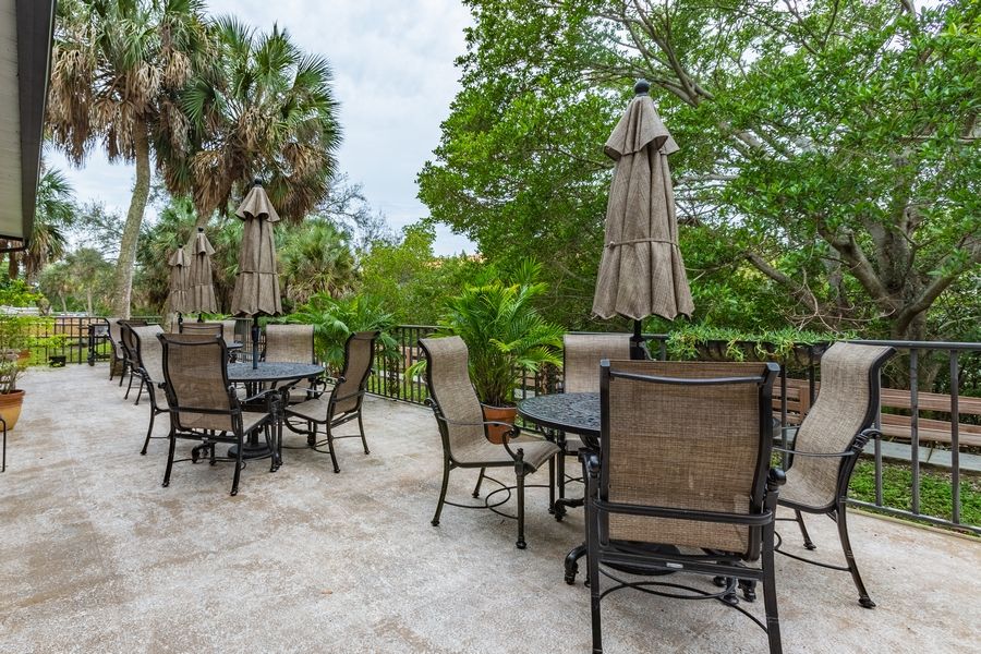 An outdoor patio with tables, chairs, and umbrellas surrounded by lush greenery.