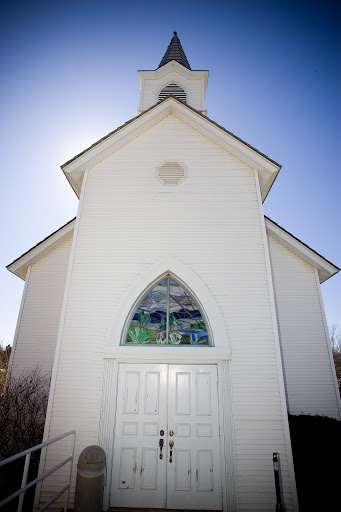 A serene white church adorned with colorful stained glass windows, basking in the bright sunlight.