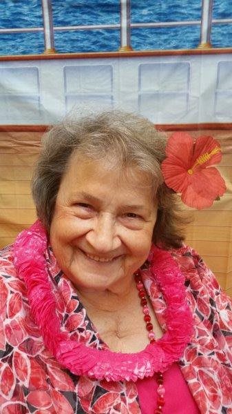 An elderly woman with a flower in her hair, wearing a Hawaiian lei and smiling warmly.