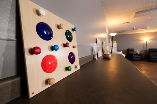 A colorful educational toy featuring various buttons on a wooden board, designed for sensory play.